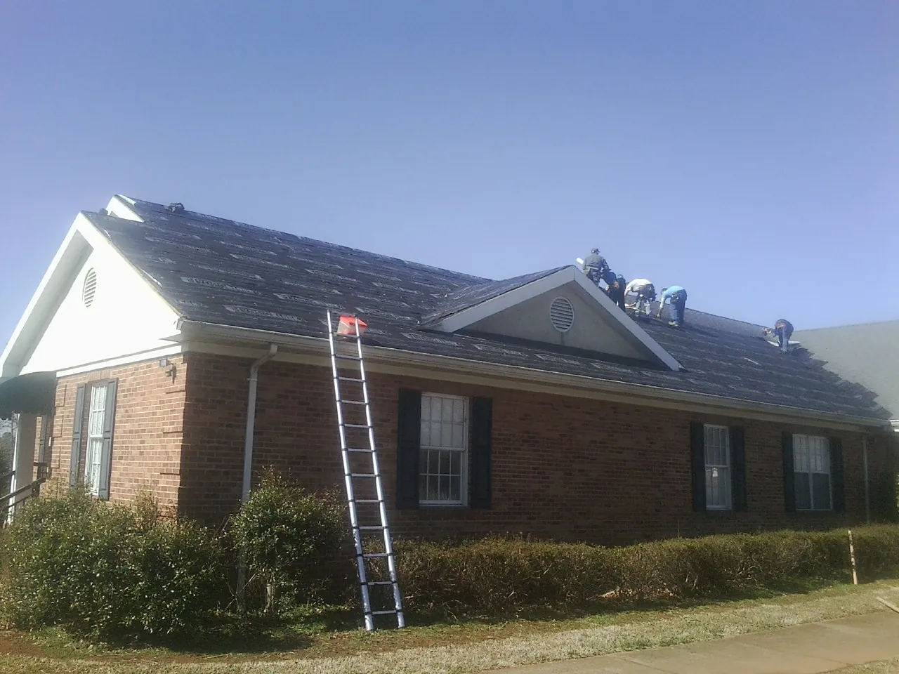 Crew tearing shingles off a brick ranch roof with a ladder set — Emergency Roof Repair work by our crew in Greencastle