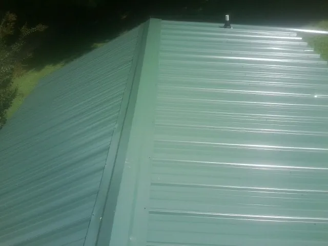 New green metal panels meeting at the ridge of a roof — Flat Roof Repair work by our crew in Greencastle