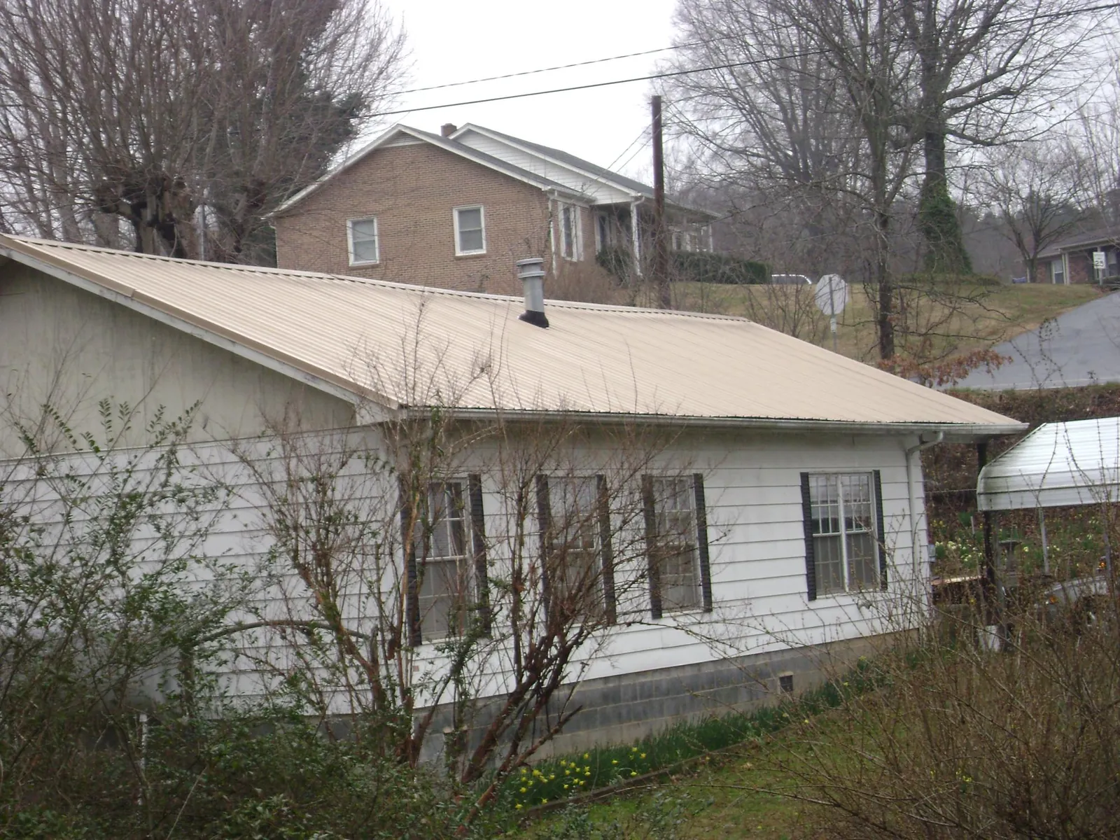 Tan metal roof on a white sided house set into a hillside — Commercial Roofing by Roofing Brothers in Greencastle